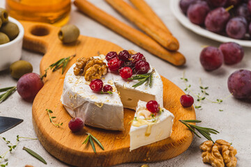 Brie cheese on a board with walnuts, honey and berries
