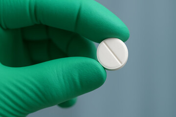Obraz premium Hand in green protective glove holding a single round white medication pill for pharmaceutical industry concept