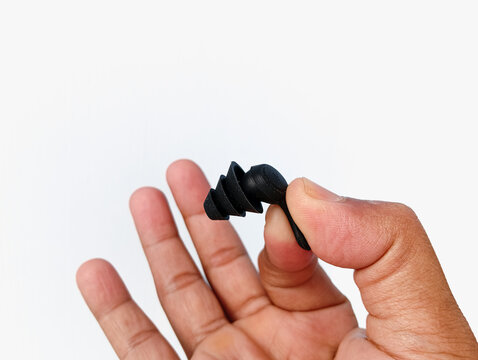Black silicone ear plug held between fingers on a clean white background, designed for noise reduction, ear protection, comfort, and reusable daily personal use.