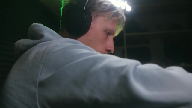 Focused young music producer wearing headphones composing electronic tracks on a synthesizer keyboard in a professional recording studio, immersed in creative sound design and workflow