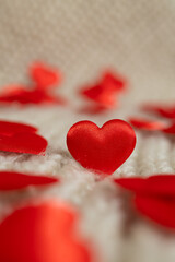 Red fabric hearts are scattered across a soft, textured white surface. The hearts vary in focus, creating a depth of field effect, perfect for Valentine's Day content.