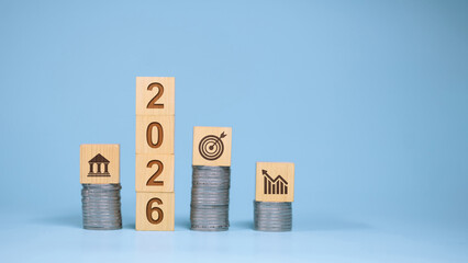 Wooden blocks with 2026 year number and coin stacks with business finance icons.