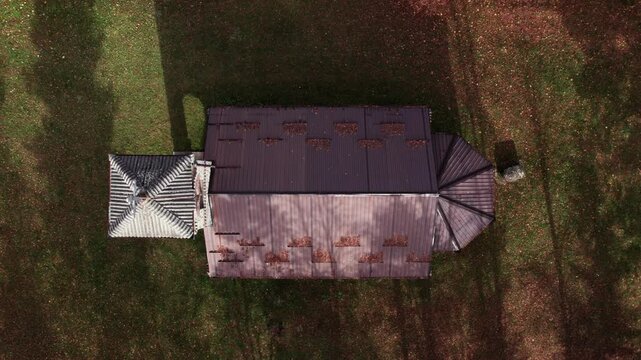 Top-down drone view of a small Orthodox stone church surrounded by autumn leaves in Turbe, Bosnia and Herzegovina. The roof and surrounding grassy landscape create a geometric, scenic composition.