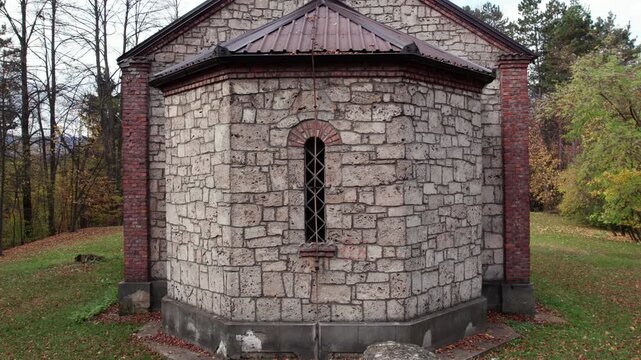 Drone view of the Orthodox church bell tower rising above the roof and autumn woodland in Turbe. Stone and brick details stand out against colorful foliage and mountain scenery.