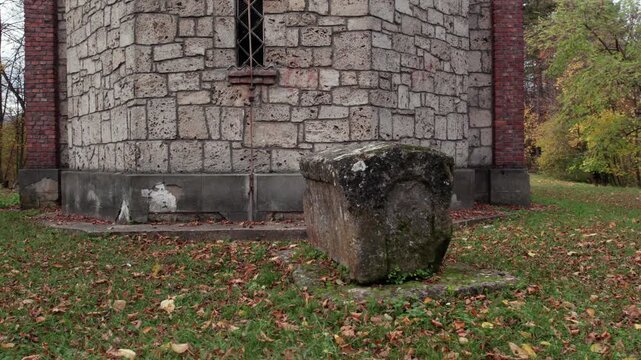 Close-up shot of an ancient stone tomb (stecak) beside the Orthodox Church of St. John the Baptist in Turbe, Bosnia and Herzegovina, surrounded by autumn leaves and historic masonry.