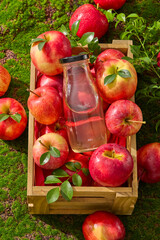 Close-up of bottle juice decorated with fresh apples arranged in a wooden crate. Green grass...
