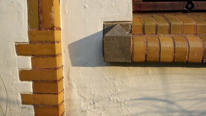 Close-up architectural detail of a white plastered wall featuring decorative yellow brickwork and a stone corner piece. Sharp geometric shadows cast by warm, natural sunlight.
