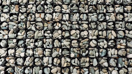 Top view of smooth grey pebbles arranged in a black plastic grid for permeable paving. A clean, modern geometric texture suitable for landscaping and architectural backgrounds.