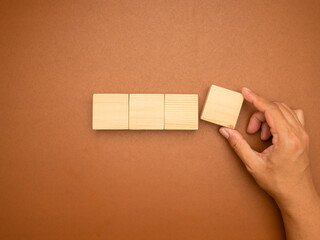 Hand arranging wooden block on brown background with copy space.
