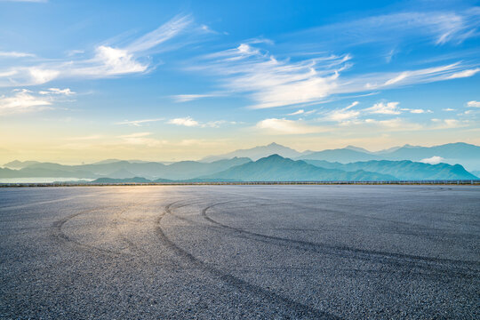 Empty asphalt race track road with tire tracks and mountain natural landscape at sunset