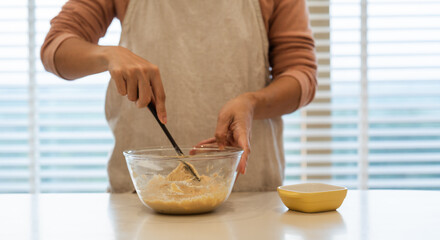 Close-up: Mixing batter in a clear bowl with a spatula on a white countertop apron on