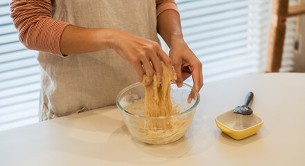 Person kneading dough in a glass bowl preparing it for baking on a clean white countertop