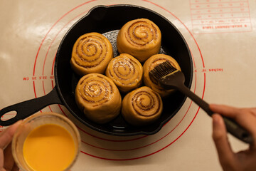 Brush applying glaze on freshly baked cinnamon rolls nestled in a cast iron skillet