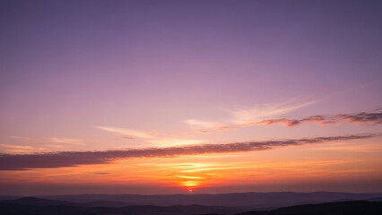 Fototapeta premium Dramatic sunset with vibrant orange and yellow hues illuminating the sky over distant rolling hills Keywords: sunset
