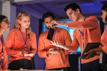 A diverse team of young innovators in a tech lab presents a new smartphone prototype,...