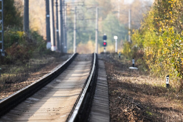 Fototapeta premium A serene railway line winds through an autumn landscape, red light is in distance