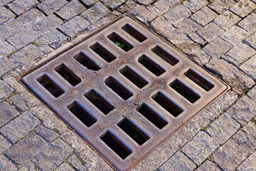 A rusty storm drain grate on a cobbled street in the old town
