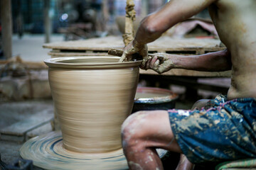 The skilled worker doing the clay work on the spinning wheel for modeling the shape of jar.