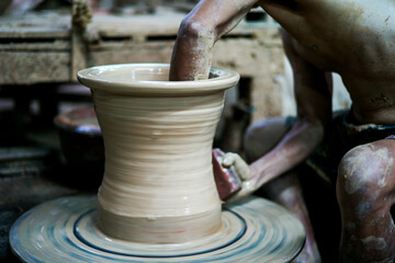 The skilled worker doing the clay work on the spinning wheel for modeling the shape of jar.