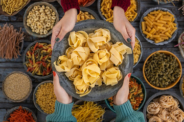 Different types of uncooked pasta at the hands of two women.