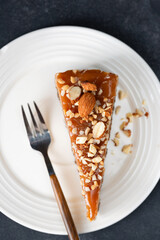 Slice of tasty caramel cheesecake with chopped almonds topping on white dessert plate