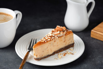 Slice of tasty caramel cheesecake with chopped almonds topping on white dessert plate