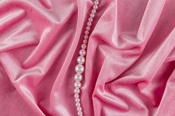 Beautiful festive background of velvet pink fabric with white pearl beads. Chic string of pearls among delicate folds of fabric material. top view.