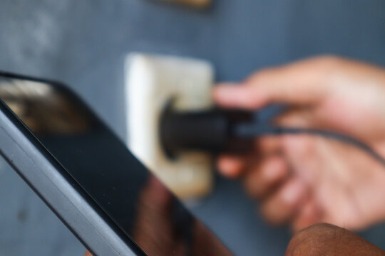 Man's hand view plugging a mobile phone charger cable into a wall socket. Ready to connect, plug in electricity