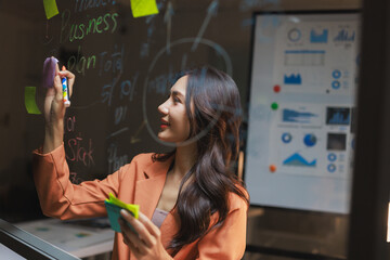 Young businesswoman brainstorming ideas on glass board