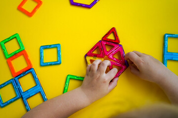 A child's creative play with magnetic construction tiles in various geometric shapes results in colorful and imaginative architectural forms.