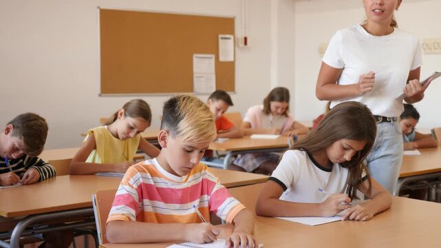  Children sitting at lesson in classroom, teacher standing