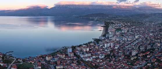 Blue hour aerial panorama of Pogradec, Albania, showing the city stretching along Lake Ohrid with soft mountain reflections on calm water.
