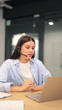 Woman engaged in a virtual video call, wearing a headset and actively communicating from office. Appears attentive and focused, dedication and helpfulness during online conference or customer support.