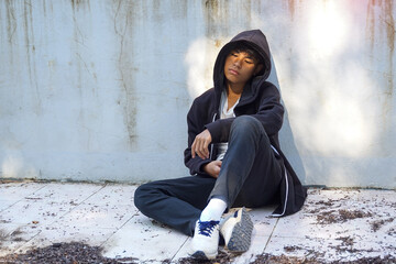 A young boy sitting alone on the ground, leaning his back against a wall, depicting feelings of loneliness, sadness, or deep thought in a quiet setting.