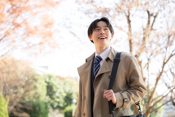 秋の紅葉の屋外でコートを着て営業の外回りなどをする男性	