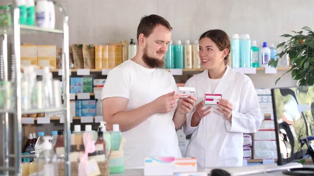 Young man buyer choosing box of paracetamol tablets with help of young woman pharmacist in pharmacy