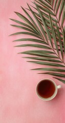 Overhead shot of a cup with dark liquid, a palm leaf fragment, all resting on a vibrant pink background. Simple, top-down perspective