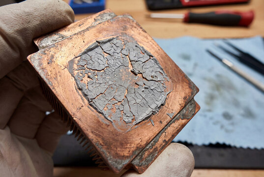 Old dried and cracked thermal paste on copper cpu cooler base held by mechanic hand