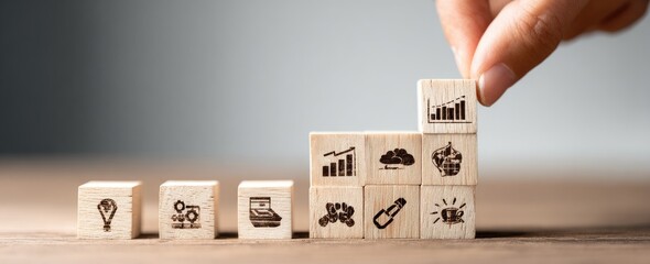 Hand placing a wooden cube with a bar chart icon atop a stack of cubes with various icon symbols