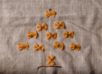 Creative Christmas tree made from bow tie pasta on linen background. Minimal food art concept and playful holiday flat lay.