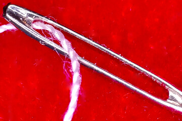 The eye of a needle with thread threaded through it.
The thread is threaded for hand sewing.
