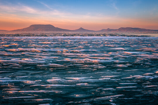 Fonyod, Hungary - Panoramic view of the frozen Lake Balaton on a cold winter afternoon with golden sunset lights and Badacsony mountain at background