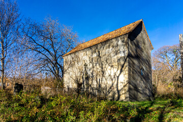A stone basilica with a tiled roof in the cemetery courtyard. Leafless trees cast shadows on the...