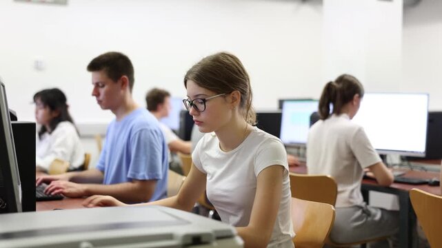 Interested young female student with glasses working on computer in university library, looking for necessary information on Internet