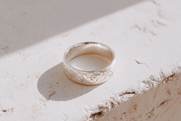 Extreme close-up of a ring with intricate engraving, focusing on metal texture and detailed patterns, soft side lighting, gentle highlights and shadows, blurred neutral background