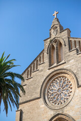 Ancient stone church facade with rose window and palm tree under blue sky