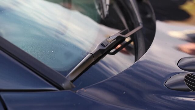 Close-up of a dark blue car windshield and wiper blades shaking from the vibration of loud music from the car's subwoofer, close-up