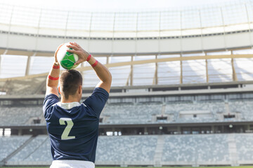 Athlete is standing on grass field holding green and white ball overhead, wearing navy jersey 2