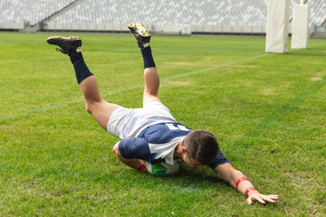 Rugby player is diving forward and is grounding green and white ball on marked grass pitch