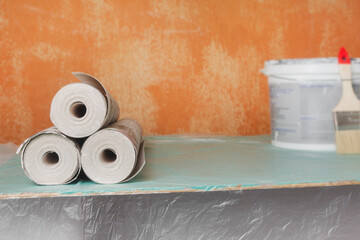 Wallpaper rolls, a brush, and paint on an old wall in a house or apartment. Concept for preparing for renovation. Copy space
